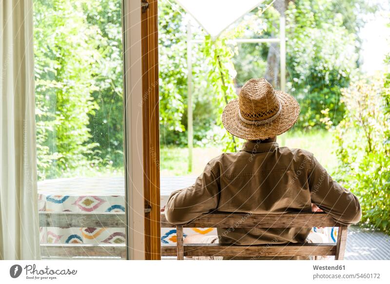 Rückenansicht eines älteren Mannes mit Strohhut auf der Terrasse, der seinen Garten genießt Deutschland Lebensabend Auszeit Alles hinter sich lassen abschalten