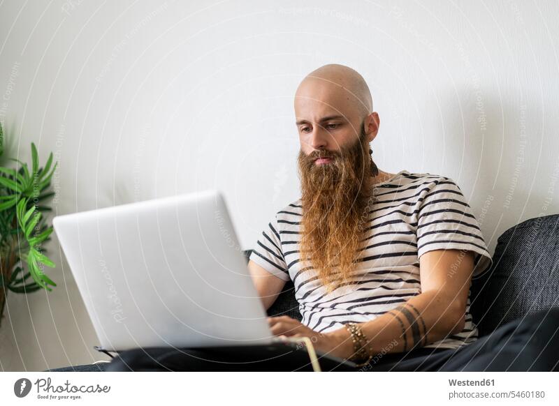 Porträt von Hipster mit Laptop zu Hause mobiles Arbeiten mobile working tätowiert Individualität Individuell Blick nach unten Freizeitkleidung casual