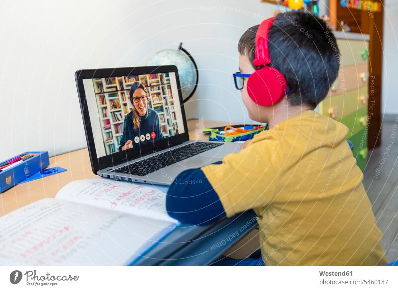 Junge hört dem Lehrer während eines Videoanrufs zu Hause über Kopfhörer zu Farbaufnahme Farbe Farbfoto Farbphoto Innenaufnahme Innenaufnahmen innen drinnen