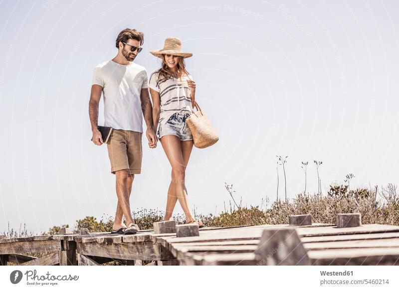 Junges Paar beim Spaziergang entlang einer Strandpromenade Touristen Taschen gehend geht Jahreszeiten sommerlich Sommerzeit entspannen relaxen entspanntheit