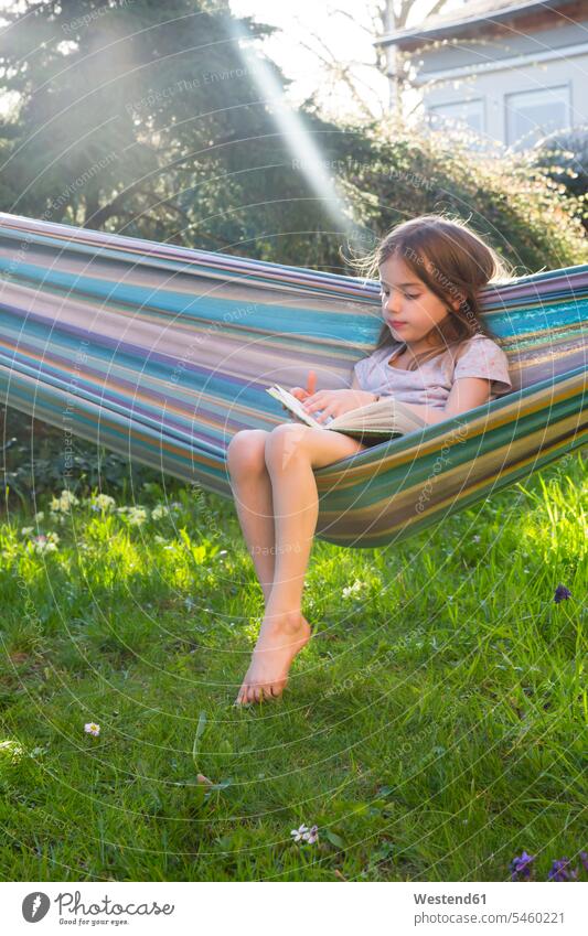 Kleines Mädchen sitzt auf einer Hängematte im Garten und liest ein Buch weiblich Gärten Gaerten Gartenanlage Gartenanlagen sitzen sitzend Kind Kinder Kids