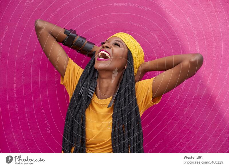Porträt einer Frau mit langen Dreadlocks lachend vor einer rosa Wand Mützen T-Shirts freuen Frohsinn Fröhlichkeit Heiterkeit Glück glücklich sein glücklichsein