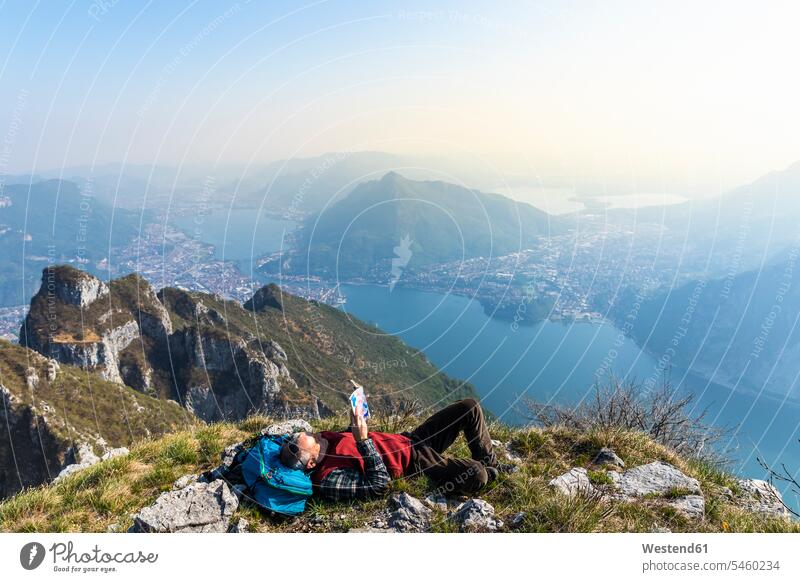 Rückansicht eines Wanderers, der ein Buch auf einem Berggipfel liest, Orobie Alps, Lecco, Italien Landschaften Berglandschaften Berge Wanderung aktiv Aktivitaet