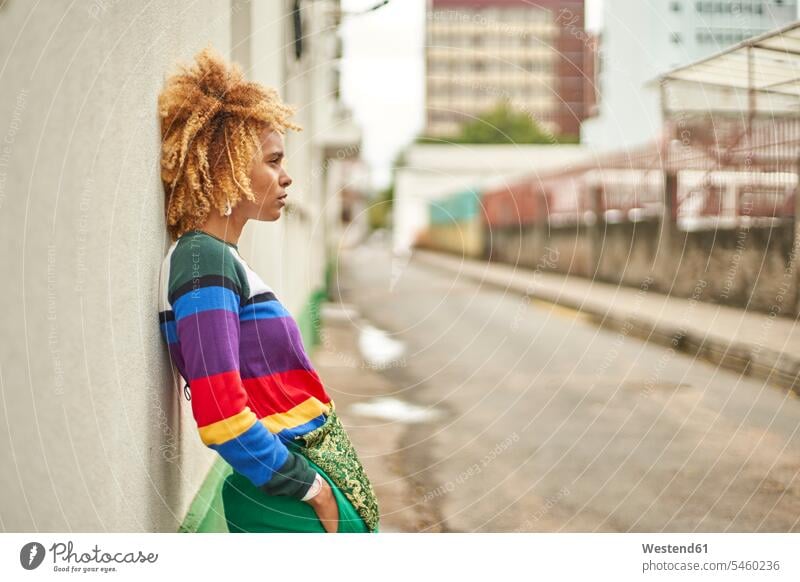 Porträt einer jungen Frau mit Afrofrisur, die an einer Mauer in der Stadt lehnt Taschen stehend steht Individuell Lifestyles außen draußen im Freien staedtisch