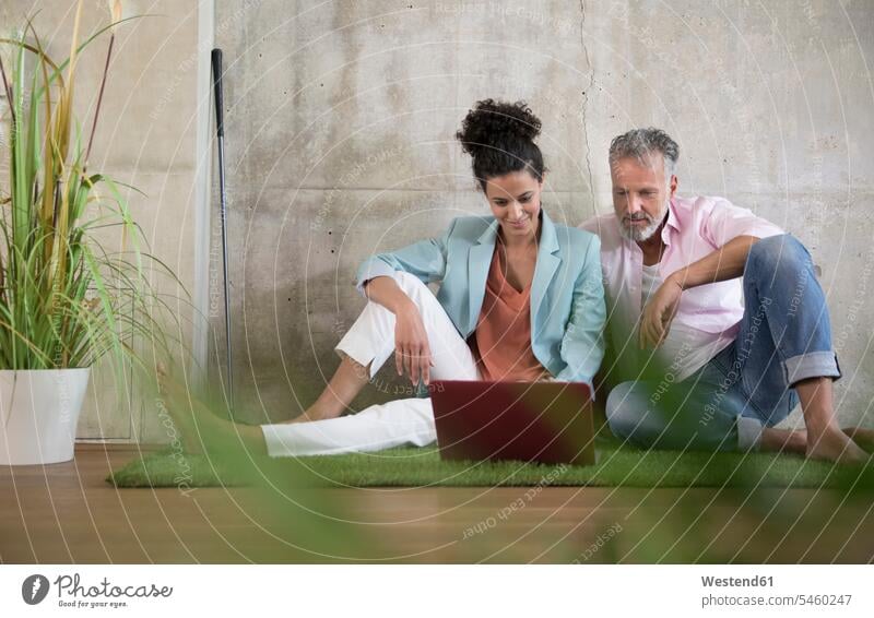 Lässiger Geschäftsmann und Geschäftsfrau sitzen auf Kunstrasen in einem Loft und teilen sich einen Laptop Businessmann Businessmänner Geschäftsmänner Notebook