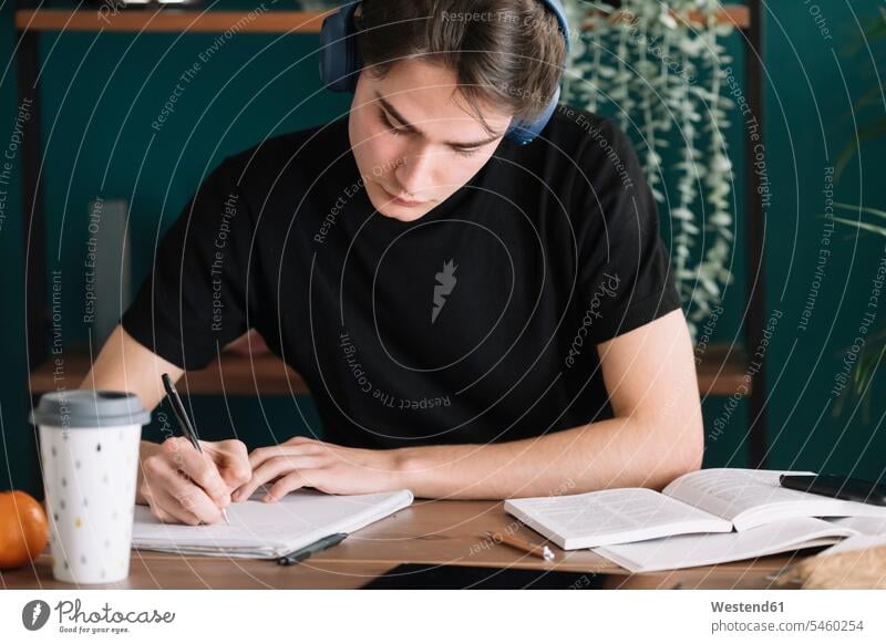 Mann schreibt in Buch, während er zu Hause über Kopfhörer Musik hört Farbaufnahme Farbe Farbfoto Farbphoto Innenaufnahme Innenaufnahmen innen drinnen Tag