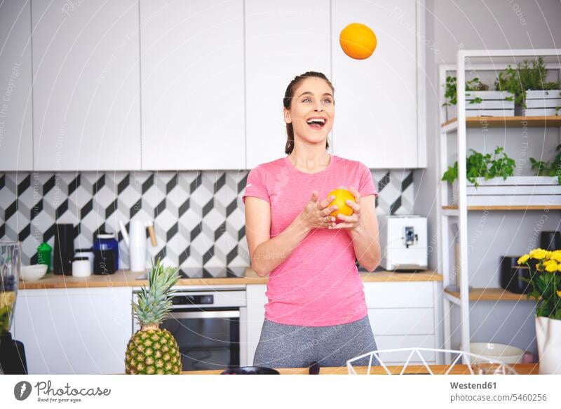 Porträt einer jungen Frau, die in der Küche mit Orangen jongliert Portrait Porträts Portraits Citrus sinensis Apfelsinen jonglieren weiblich Frauen Küchen