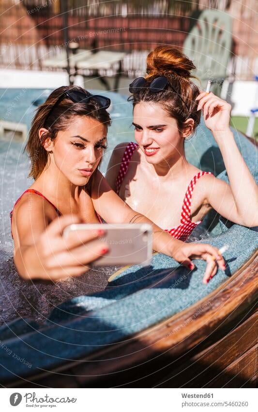Zwei Frauen machen ein Selfie in einem Jacuzzi Freunde Kameradschaft Freundin Bilder Bildnis Fotos Tabak Zigaretten Badebekleidung Bikinis Telekommunikation