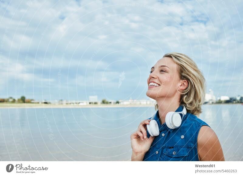Deutschland, Düsseldorf, glückliche junge Frau mit Kopfhörer am Rheinufer Kopfhoerer weiblich Frauen Glück glücklich sein glücklichsein Fluss Fluesse Fluß