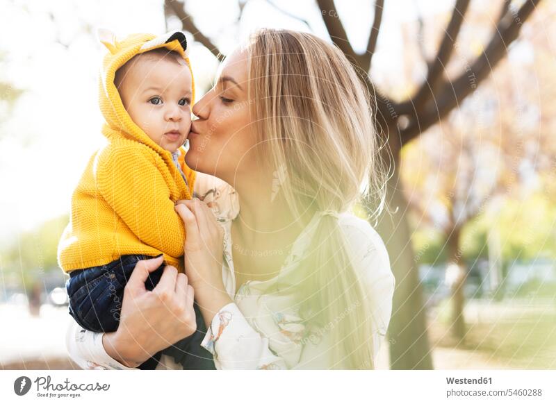 Mutter küsst einen kleinen Jungen in einem Park Jacken knuddeln schmusen Kuss Küsse Arm umlegen Umarmung Umarmungen freuen behüten behütet geborgen Sicherheit