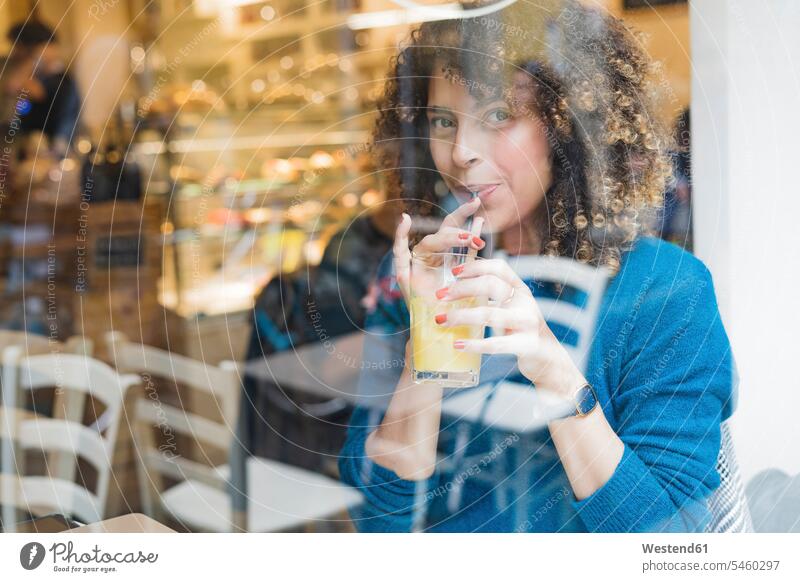 Porträt einer Frau, die in einem Cafe hinter einer Fensterscheibe einen Smoothie trinkt Leute Menschen People Person Personen gelockt gelockte Haare