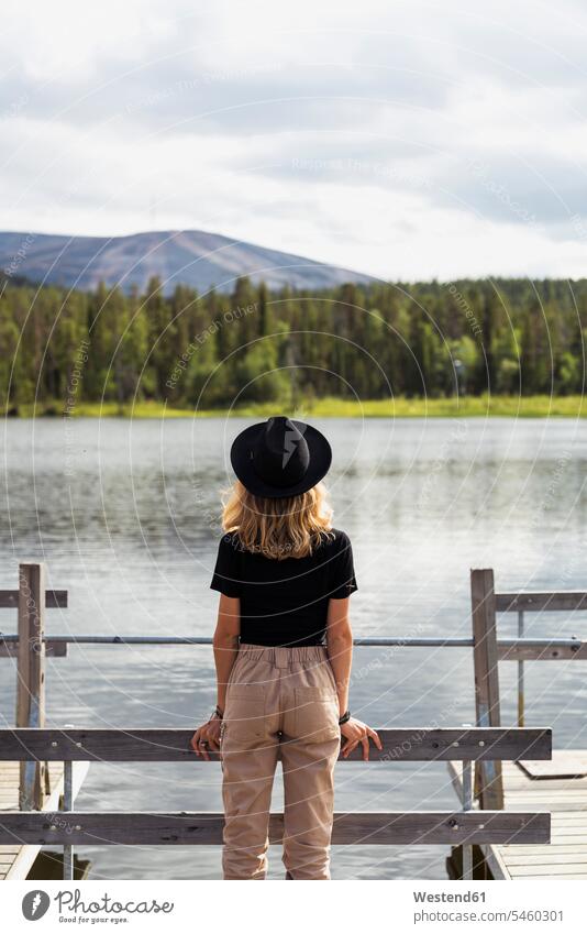 Finnland, Lappland, Frau mit Hut auf einem Steg an einem See stehend Seen Hüte Stege Anlegestelle steht weiblich Frauen Gewässer Wasser Erwachsener erwachsen
