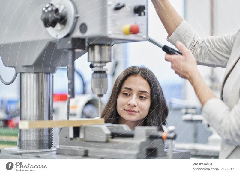 Ausgeschnittenes Bild eines Managers, der Metall bohrt, während er weibliche Arbeitskräfte in der Metallindustrie ausbildet Farbaufnahme Farbe Farbfoto