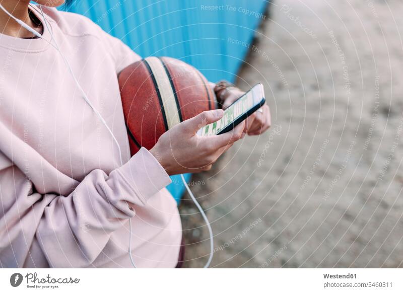 Nahaufnahme einer Frau mit Basketball, Smartphone und Kopfhörern Ohrhörer Basketbaelle Basketbälle weiblich Frauen iPhone Smartphones In-Ear Kopfhoerer Sport