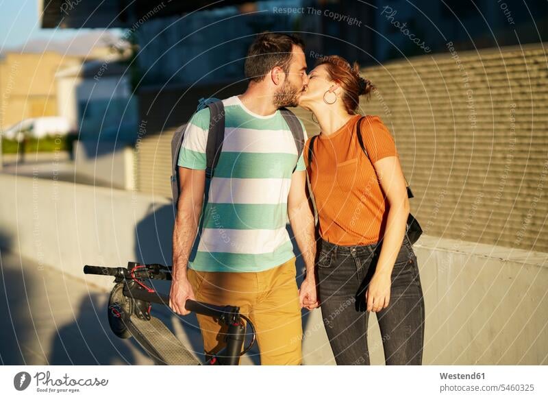 Küssendes Paar mit gefaltetem Elektroroller Leute Menschen People Person Personen Europäisch Kaukasier kaukasisch 2 2 Menschen 2 Personen zwei Zwei Menschen