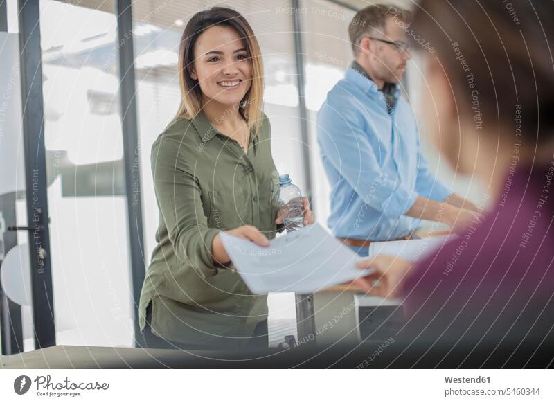 Lächelnde Geschäftsfrau im Büro übergibt Papier an Kollegin Dokument Dokumente Papiere Unterlagen Geschäftsfrauen Businesswomen Businessfrauen Businesswoman