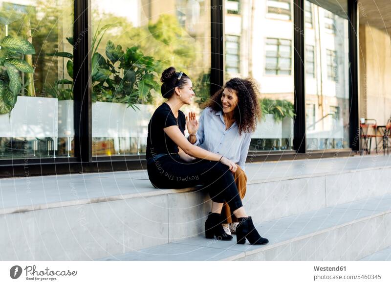 Zwei Freundinnen sitzen auf den Stufen und tratschen Freunde Kameradschaft sitzend sitzt reden freuen Spass spassig spaßig Spässe Späße außen draußen im Freien