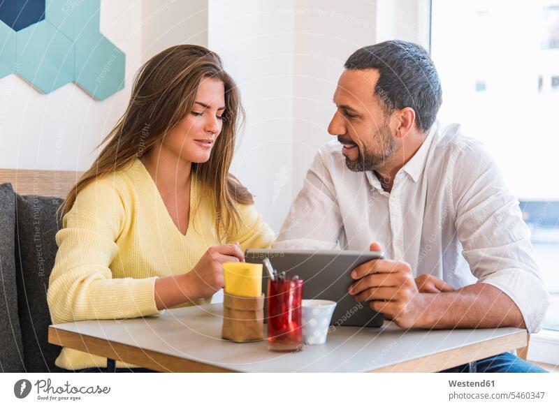 Junge Frau und Mann teilen sich Tabletten in einem Café Männer männlich Cafe Kaffeehaus Bistro Cafes Cafés Kaffeehäuser Teilen Sharing weiblich Frauen