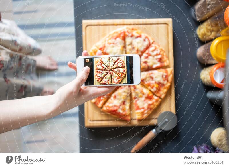 Ausschnittansicht einer Frau, die eine selbstgemachte Pizza mit einem Smartphone fotografiert Handies Handys Mobiltelefon Mobiltelefone Displays stehend steht