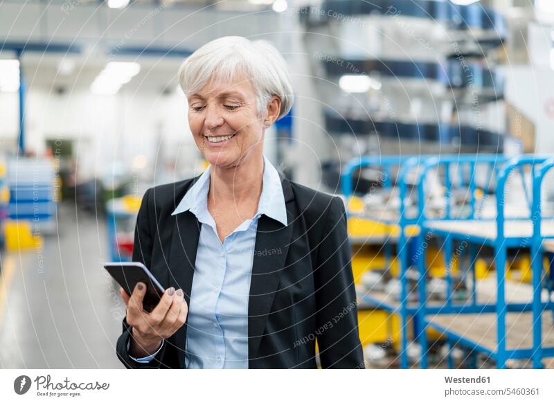 Lächelnde ältere Geschäftsfrau schaut auf Handy in einer Fabrik Mobiltelefon Handies Handys Mobiltelefone ansehen Fabriken Geschäftsfrauen Businesswomen