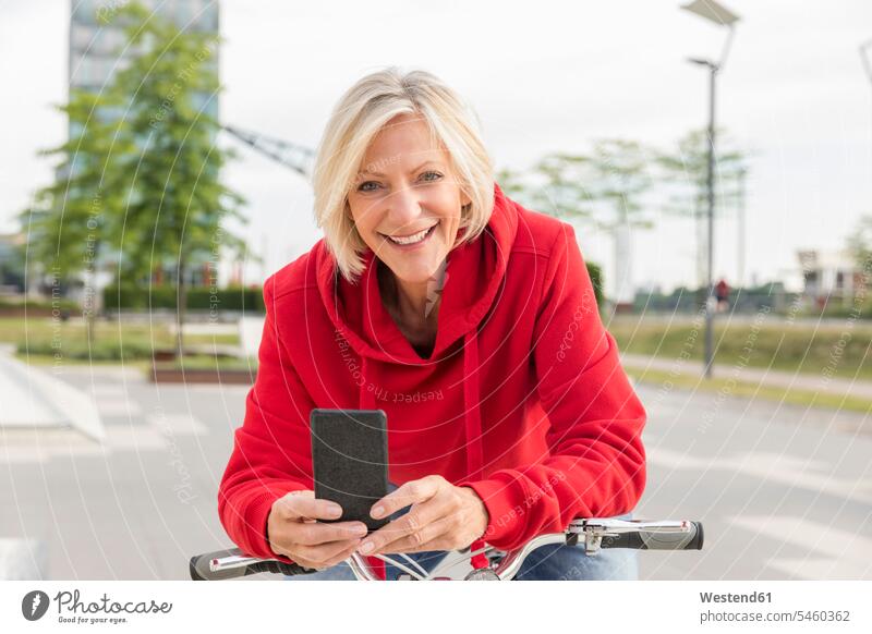 Porträt einer lächelnden älteren Frau mit Stadtfahrrad und Mobiltelefon Fahrrad Bikes Fahrräder Räder Rad Portrait Porträts Portraits Zuversicht Zuversichtlich