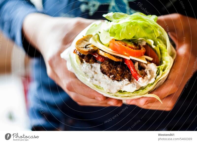 Eine Person hält an den Händen einen Low-Carb-Burger mit Brötchensalat, gebratenem Gemüse und Tzatziki-Sauce Nahaufnahme close up close-up close ups close-ups