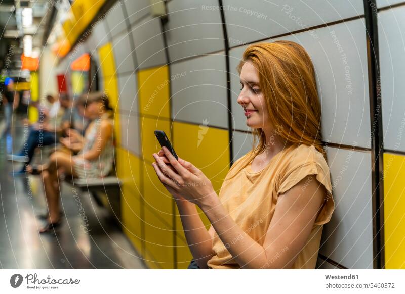 Frau benutzt Smartphone in U-Bahn-Station T-Shirts Telekommunikation telefonieren Handies Handys Mobiltelefon Mobiltelefone sitzend sitzt freuen Glück