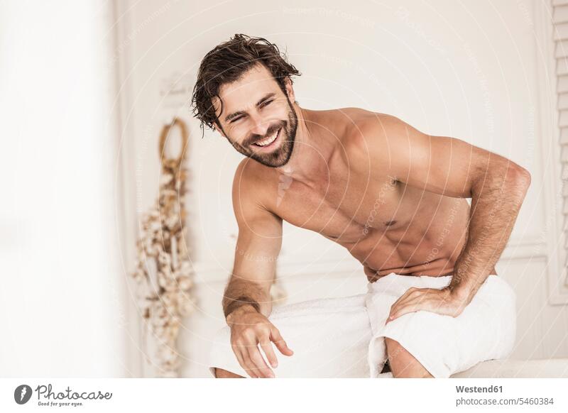 Junger Mann ohne Hemd in einem Badezimmer Badewannen Handtuecher Handtücher Bademäntel Betten entspannen relaxen sitzend sitzt früh Frühe Morgen freuen Frohsinn