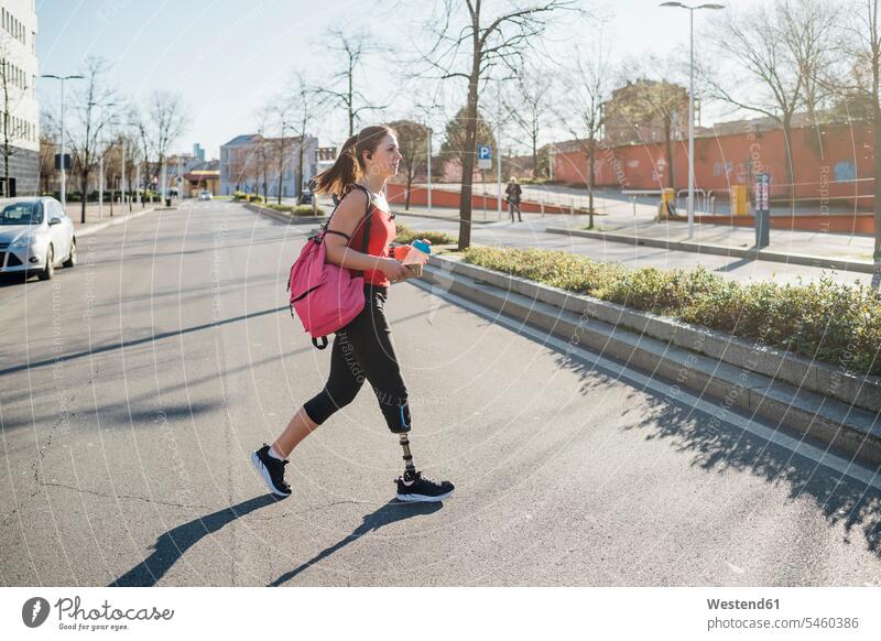 Sportliche junge Frau mit Beinprothese beim Spaziergang in der Stadt Rucksäcke gehend geht Farben Farbtoene Farbton Farbtöne pinkfarben rosa rote roter rotes