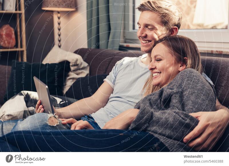 Glückliches junges Paar mit Tablet auf der Couch zu Hause entspannt entspanntheit relaxt Pärchen Paare Partnerschaft Sofa Couches Liege Sofas Tablet Computer