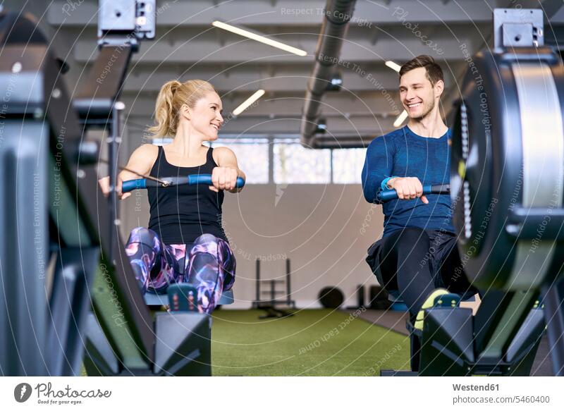 Mann und Frau im Fitnessstudio üben gemeinsam an Rudergeräten Fitnessclubs Fitnessstudios Turnhalle Männer männlich weiblich Frauen Rudergeraet Rudergeraete fit