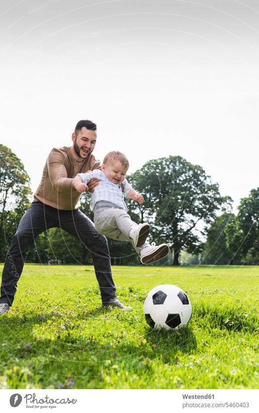 Glücklicher Vater spielt mit seinem Sohn in einem Park Fussball Söhne Parkanlagen Parks glücklich glücklich sein glücklichsein aktiv Papas Väter Vati Vatis