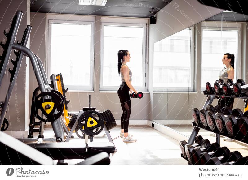 Frau hebt Kurzhanteln im Fitnessstudio und schaut in den Spiegel Fitnessclubs Fitnessstudios Turnhalle schauen sehend weiblich Frauen Hantel Hanteln heben fit