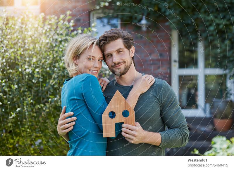 Porträt des glücklichen Paares vor ihrem Haus mit Hausmodell Modell Modelle Portrait Porträts Portraits Häuser Haeuser Pärchen Partnerschaft Glück