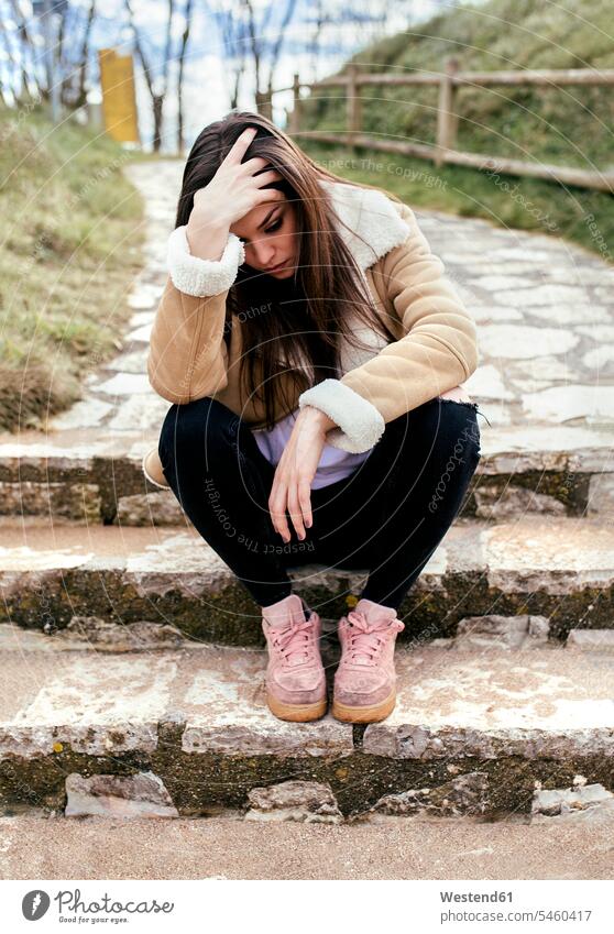 Traurige junge Frau sitzt im Freien auf Stufen schön traurig braune Haare braunhaarig brünett braunes Haar Treppe Treppenstufe Treppenstufen sitzen sitzend