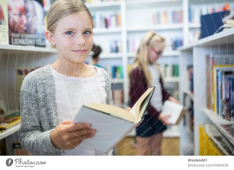 Porträt eines lächelnden Schulmädchens mit Buch in der Schulbibliothek Bücher Schülerin Schuelerin Schülerinnen Schuelerinnen Schule Schulen Bücherei Schulkind