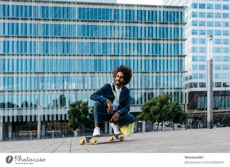 Spanien, Barcelona, junger Geschäftsmann hockend auf Skateboard in der Stadt Businessmann Businessmänner Geschäftsmänner staedtisch städtisch Mann Männer