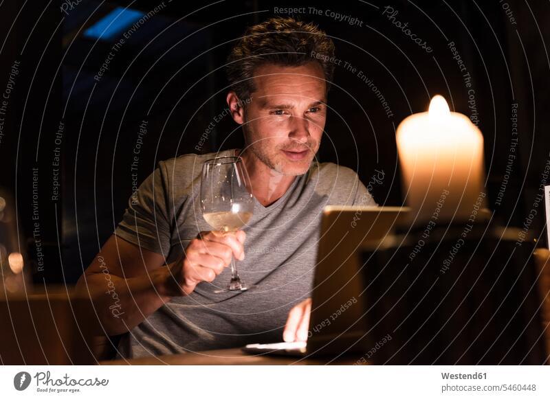 Mann bei einem Glas Weißwein mit Blick auf Laptop Wein Weine Notebook Laptops Notebooks ansehen Männer männlich Dinner Alkohol Alkoholische Getraenke