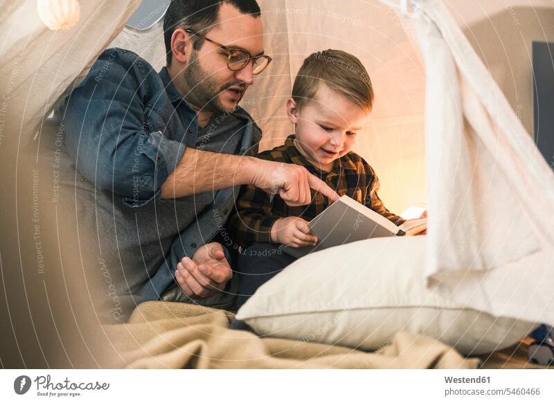 Vater und Sohn lesen gemeinsam ein Buch im Zelt zu Hause Bücher Zelte Lektüre Söhne Gemeinsam Zusammen Miteinander Papas Väter Vati Vatis Papis Zuhause daheim