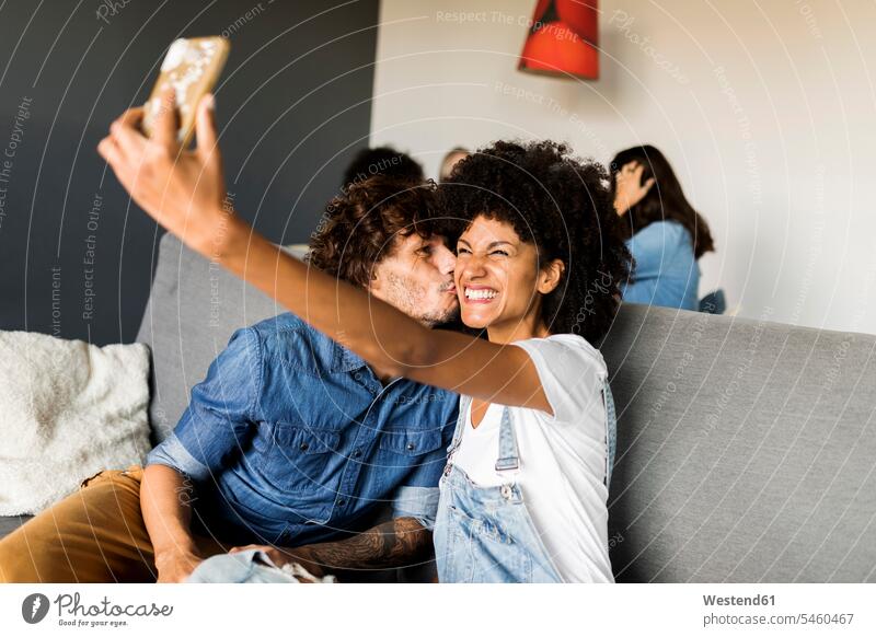 Glückliches Paar sitzt auf der Couch und macht ein Selfie Selfies sitzen sitzend glücklich glücklich sein glücklichsein Pärchen Paare Partnerschaft Sofa Couches