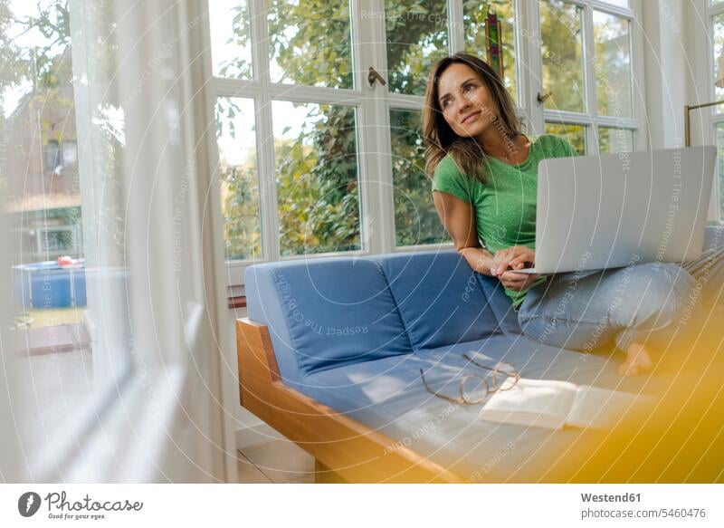 Lächelnde reife Frau sitzt auf der Couch zu Hause mit Laptop Zuhause daheim sitzen sitzend lächeln Notebook Laptops Notebooks weiblich Frauen Sofa Couches Liege