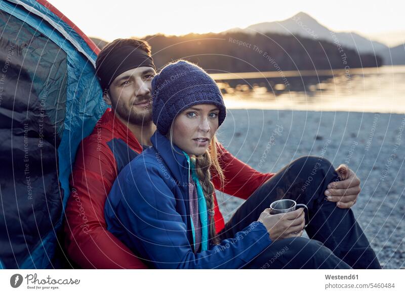 Junges Paar sitzt im Zelt am Seeufer Pärchen Paare Partnerschaft sitzen sitzend Zelte Seen Mensch Menschen Leute People Personen Gewässer Wasser Ufer
