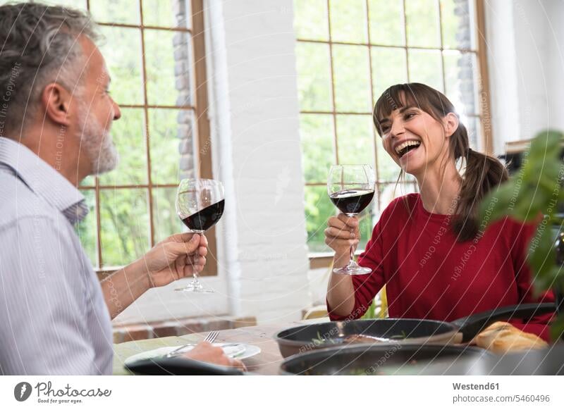 Glückliches Paar sitzt in der Küche, trinkt mit Rotwein und genießt das Abendessen trinken anstoßen zuprosten anstossen Pärchen Paare Partnerschaft sitzen