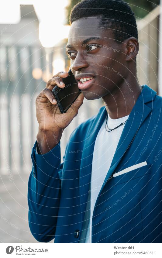 Junger Geschäftsmann im Blazer, der im Freien mit einem Mobiltelefon telefoniert Farbaufnahme Farbe Farbfoto Farbphoto Außenaufnahme außen draußen Tag