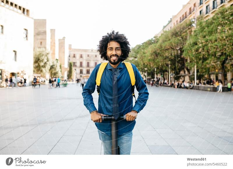 Porträt eines lächelnden Mannes mit Rucksack auf seinem E-Scooter nach der Arbeit, Barcelona, Spanien Rucksäcke Businesskleidung Krawatten Schlips Schlipse