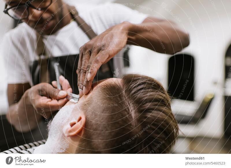 Mann lässt sich beim Friseur den Bart mit einem Rasiermesser rasieren Leute Menschen People Person Personen Afrikanisch Afrikanische Abstammung dunkelhäutig