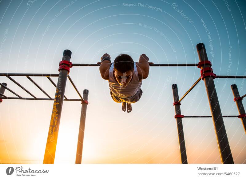 Junger Mann übt bei Sonnenaufgang Gymnastik in einer Turnhalle im Freien Leute Menschen People Person Personen Europäisch Kaukasier kaukasisch 1 Ein ein Mensch