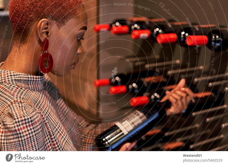 Junge Frau mit kurzem Haarschnitt wählt einen Wein in ihrem Keller Leute Menschen People Person Personen Afrikanisch Afrikanische Abstammung dunkelhäutig