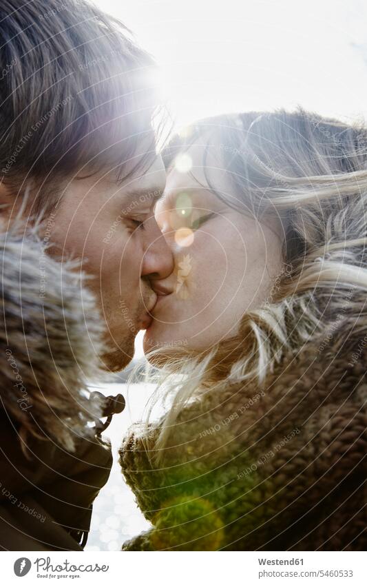 Küssendes junges Paar im Winter bei Gegenlicht Kuss abends Jahreszeiten winterlich Winterzeit Glück glücklich sein glücklichsein gefühlvoll Emotionen Empfindung