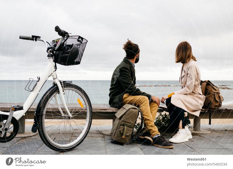 Paar sitzt auf einer Bank an der Strandpromenade neben dem E-Bike und schaut auf das Meer eBikes E-Bikes Elektrofahrrad Elektrorad Pause Meere Pärchen Paare